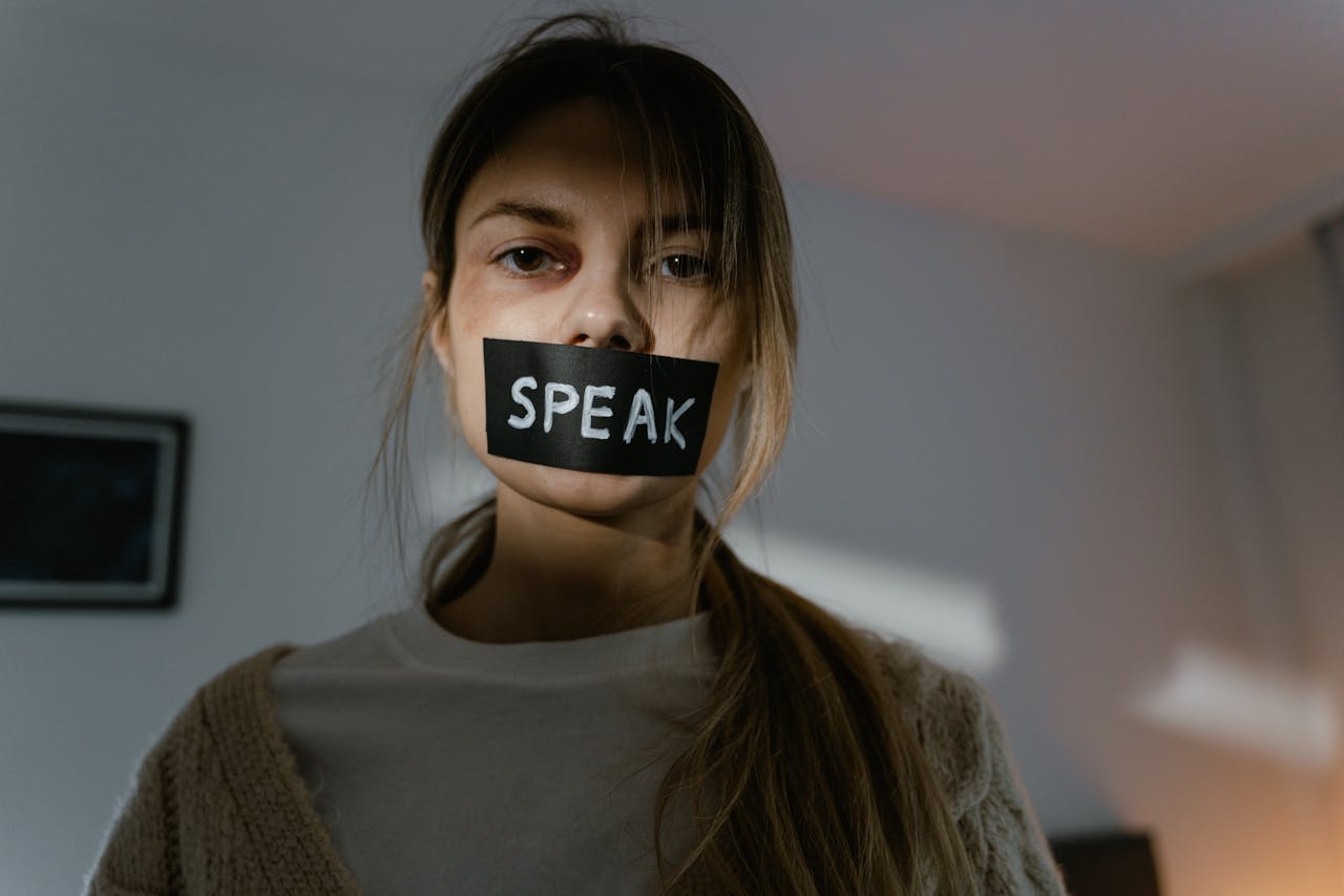 Woman with 'speak' tape over mouth highlights domestic abuse issues.